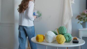 in de voorgrond, Daar zijn kleurrijk ballen van garen. een van hen is tot rust komen en vallend uit de tafel. de jong ontwerper is verloofd in creëren tapijten. medium schot. langzaam beweging. 4k. video