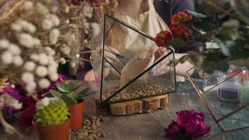 Florist carefully pours sand into the glass hexagonal container, on top of the expanded clay. The beautiful flower shop and workshop. Close up. Slow motion. 4k video