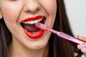 recortado ver de contento mujer limpiar dientes por cepillar. morena mujer posando a el estudio con cepillo a su boca dama tomando cuidado de su dientes después blanqueo. procedimientos para Perfecto sonrisa concepto foto