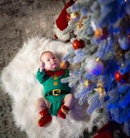 Top view of the sweet baby lying on the floor in a costume of elf. Baby near the fur tree at the new year. Side view. photo