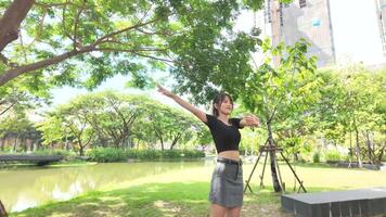 ásia menina dançando e torcendo, comovente dela braços dentro a parque durante a dia video