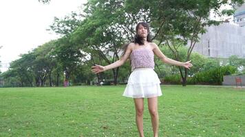 asiático niña bailando y aplausos, Moviente su brazos dentro el parque durante el día video