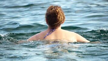 Woman swimming in calm sea at sunset, slow-motion, back view. Concept of body image and fitness, enjoying a serene beach. Happy woman with perfect fit body enjoys sea beach video