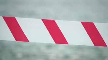 Red white warning tape barrier ribbon swinging in the wind across exotic sea beach background without people. No entry Red White caution tape. No holiday concept, delayed travel, no summer plans video