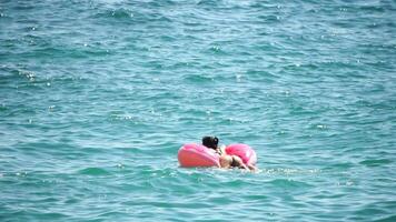 verano vacaciones mujer flotadores en un inflable rosquilla colchón, un agua juguete nadar anillo. positivo contento mujer relajante y disfrutando familia verano viaje Días festivos vacaciones en el mar. lento movimiento video