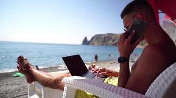 hombre ordenador portátil mar. trabajando remotamente en costa. contento exitoso hombre, masculino persona de libre dedicación trabajando en ordenador portátil en playa, alivia estrés desde trabajo a restaurar vida balance. Lanza libre, remoto trabajo en vacaciones video