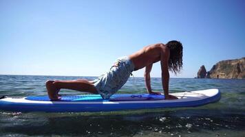 uomo cenare yoga. contento sportivo uomo praticando yoga pilates su pagaia cenare tavola da surf. maschio allungamento fare allenarsi su mare acqua. moderno individuale maschio fricchettone all'aperto estate sport attività. video
