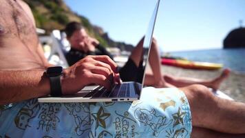 Man laptop sea. Working remotely on seashore. Happy successful man, male freelancer working on laptop on beach, relieves stress from work to restore life balance. Freelance, remote work on vacation video