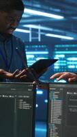 Vertical Engineers working in high tech server farm, using laptop and tablet to analyze data, ensuring seamless data flow. Men examining hardware in data center, ensuring system integrity and security video