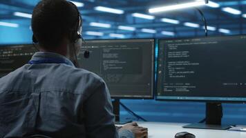 IT support worker in data center talking in headset mic with coworkers, coding on computer. Man discussing with colleagues using headphones microphone, overseeing server clusters video