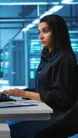 Vertical Computer scientist working in high tech server hub capable of processing vast amounts of data. Woman at PC desk typing on keyboard, updating servers controlling network resources video