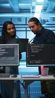 Vertical Multiracial colleagues in server hub workspace collaborating to fix servers providing computing resources for workloads. Engineers doing brainstorming while supervising data center supercomputers video