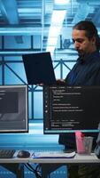 vertikal mitten östra chef i server nav arbetsplats håller på med inspektion på elektronik och raser arbetare. team ledare läsning pappersarbete på bärbar dator, verifierande infrastruktur dokument, håller på med granska video