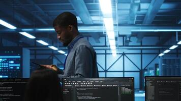 Engineer inputting data on tablet in server hub, monitoring data center energy consumption across hardware. Technician inspecting mainframes, ensuring malfunctions are repaired video