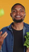 Vertical Cheerful person juggling with a green ripe apple on camera, carrying paper bag full of organic bio groceries. Smiling young man playing around with a fruit, sustainable lifestyle. Camera A. video