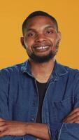 Vertical Portrait of african american casual man posing against orange background, showing confidence and determination in studio. Charismatic serious guy in stylish clothes. Camera A. video