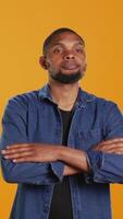 Vertical Portrait of confident person smiling on camera against orange background, posing with arms crossed in studio. Enthusiastic happy man feeling relaxed and cool, masculine figure. Camera B. video