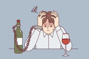 Man suffering from alcohol addiction is chained to bottle of wine, sitting at table clutching head vector