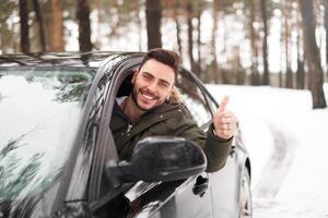 joven atractivo caucásico hombre se sienta a el rueda de su coche soleado invierno día. foto