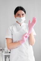 Cosmetologist in mask putting on pink gloves in beauty clinic photo