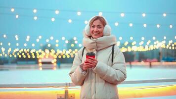 Woman in warm clothes with takeaway coffee outside ice rink during Christmas video