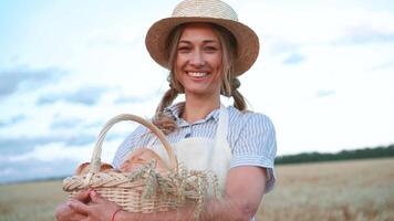 Happy female baker holding wicker basket full of fresh bread loaves on farm. video