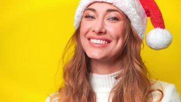 Happy woman wearing Santa hat smiling over plain yellow background video