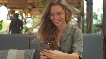 sonriente mujer utilizando teléfono inteligente a mesa a café terraza video