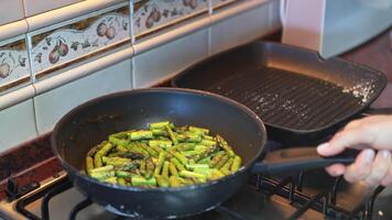 Hand tossing asparagus pieces being fried in pan on stove video