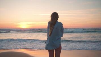 zorgeloos vrouw staand Aan kust Bij winderig strand gedurende zonsondergang video