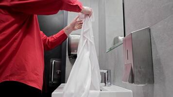 Man washing hands in public restroom, A man in a red shirt is washing his hands in a public restroom. video