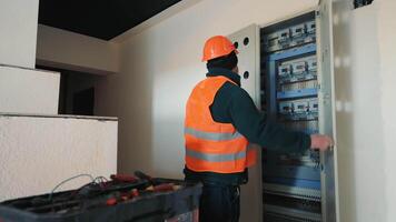 elettricista Lavorando su un' pannello, un elettricista nel un' sicurezza veste e difficile cappello è Lavorando su un elettrico pannello. video