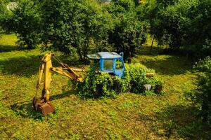 An old tractor with a bucket, abandoned from a green garden photo