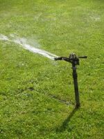 Sprinkler Spraying Water On Green Grass Lawn At Park photo