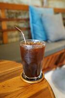 cerca arriba vaso de con hielo negro café en de madera mesa foto