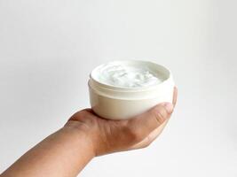 Close up of childs hand holding container of cream on white background with copy space. Skincare and moisturizing concept. Design for healthcare, wellness, and child care poster. photo