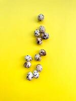 Speckled quail eggs arranged on bright yellow surface, flat lay design ideal for themes of Easter, healthy eating, and springtime festivities. photo