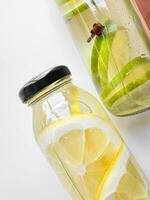 Close up of detox drinks lemon and lime in glass bottles on white background. Macro photography with focus on the foreground, healthy beverage concept for design and print. photo