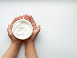 Close up of childs hands holding container of hand cream on white background with copy space. Skincare and moisturizing concept. Design for healthcare and wellness. photo