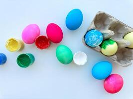 Vividly painted Easter eggs scattered beside open cans of colorful paint and an egg carton on light white background, festive DIY concept with space for text. photo