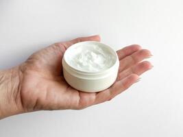 Close up of middle age woman hand holding container of hand cream on white background. Skincare and moisturizing concept. Design for healthcare, beauty, wellness, and self care poster. photo