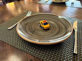 Miniature taxi toy on ceramic plate with cutlery. Concept of calling taxi after end of banquet or celebration. Design of taxi advertising, culinary presentations and unusual concepts. photo