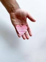 Mans hand holding striped pink paper heart against white background, symbolizing love and care, with copy space. Can be used for design and print related to childrens, love and relationships themes photo