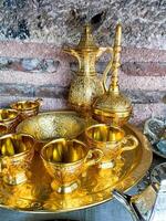 Vintage golden tea set with intricate designs on tray against rustic stone wall. Traditional ornate metalware concept for interior design and decoration. photo