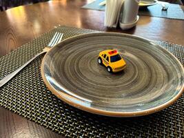 Miniature taxi toy on ceramic plate with cutlery. Concept of calling taxi after end of banquet or celebration. Design of taxi advertising, culinary presentations and unusual concepts. photo