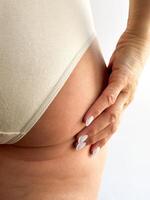 Close up of womans hand with white nails resting on her hip, wearing beige underwear. Focuses on skincare, body care, and personal hygiene, highlighting healthy skin and well groomed nails. photo