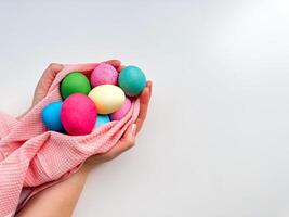 Hands tenderly hold variety of colorful Easter eggs wrapped in soft pink fabric on white background with empty space for text. Suitable for seasonal celebrations and festive spring looks. photo