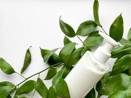 Close up of white lotion bottle surrounded by green leaves on white background. Skincare and natural beauty concept. Design for healthcare, wellness, and organic product poster. photo