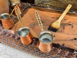 Traditional Turkish coffee in copper turks with long handles on tray with sand. Real coffee preparation, close up with selective focus. photo
