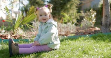 Cute child girl in backyard garden sitting and playing on lawn. video